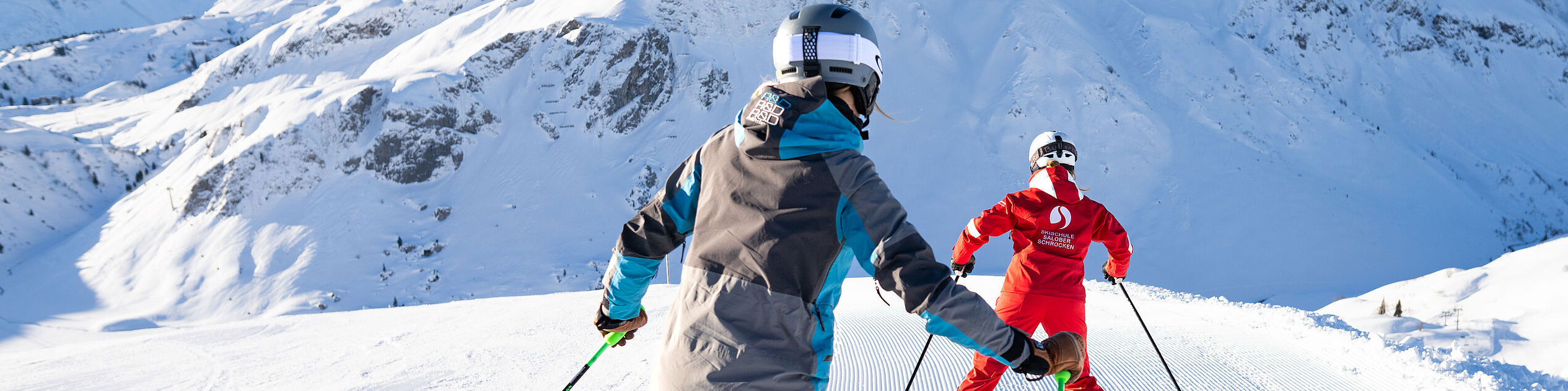Eine Skischülerin fährt ihrer Skilehrerin auf der Piste nach