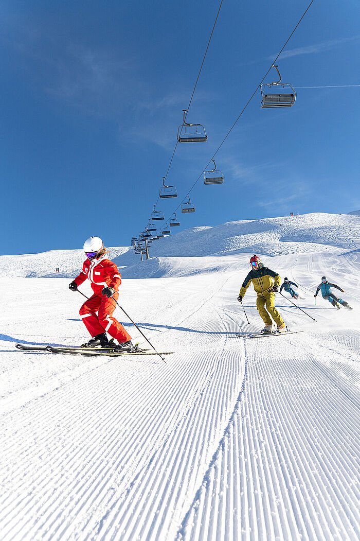 Eine Gruppe fortgeschrittener Skifahrer fährt dem Skilehrer nach