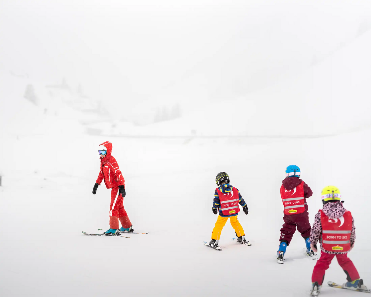 Drie kinderen volgen hun skileraar tijdens een kinderskicursus