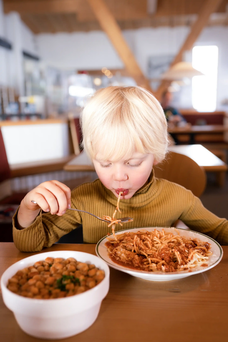 Een kind zit in het restaurant en eet spaghetti met saus