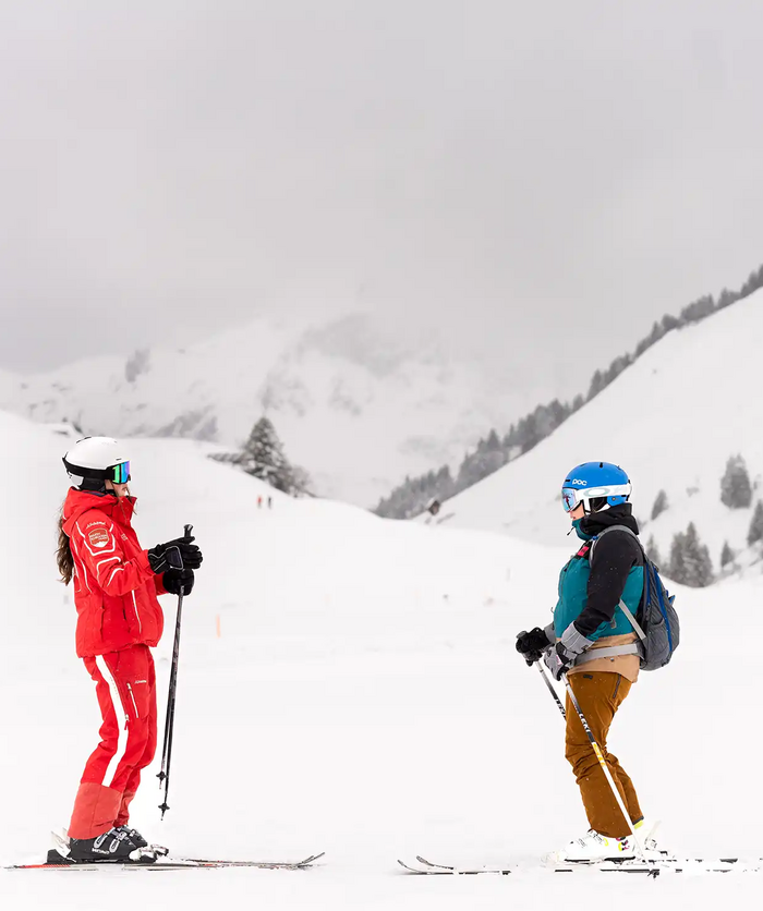 Een skilerares van de skischool Salober-Schröcken en een jonge cursist staan tegenover elkaar op de piste en praten met elkaar.