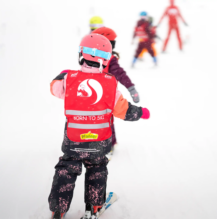 Een groep kleine kinderen skiet achter elkaar aan tijdens een skicursus